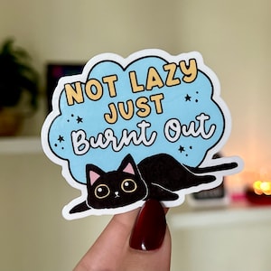 May include: A blue and white sticker with a black cat and the text "Not Lazy Just Burnt Out".