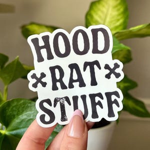May include: A white sticker with black text that reads "HOOD *RAT* STUFF".