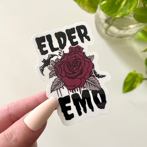 May include: A black and white sticker with the text "Elder Emo" in a gothic font. A red rose with dripping blood and a bat are featured in the design.