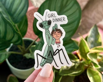 Può includere: Una mantide religiosa verde con grandi occhi tiene una testa umana tra le mani. La testa sanguina e la mantide ha il testo "Girl Dinner" scritto sopra.
