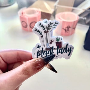 May include: A white sticker with a black and green illustration of potted plants and the text "plant lady".