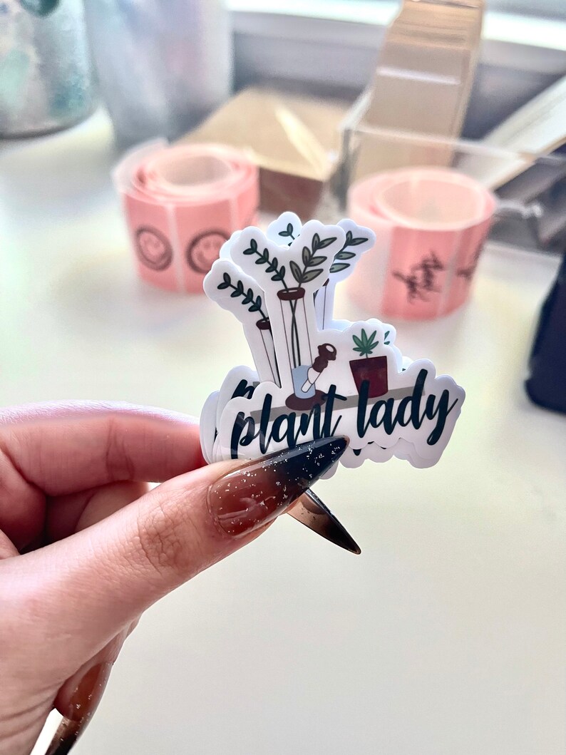 May include: A white sticker with a black and green illustration of potted plants and the text "plant lady".