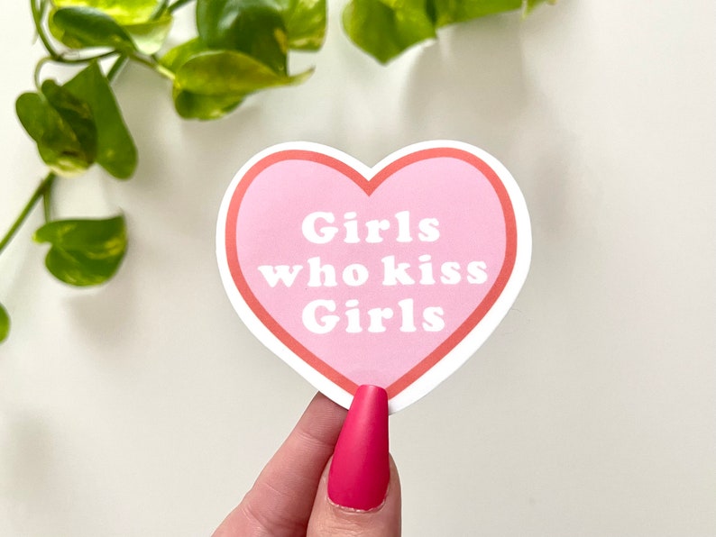 Puede incluir: Pegatina rosa en forma de coraz&oacute;n con el texto "Girls who kiss Girls" en blanco.