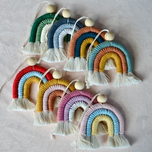 May include: A set of eight rainbow-colored macrame wall hangings with wooden beads. Each hanging features a different color combination of yarn, creating a vibrant and colorful display.