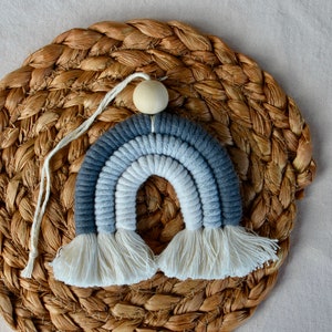 May include: A blue and white ombre rainbow wall hanging with white tassels. The rainbow is made of yarn and has a wooden bead at the top.
