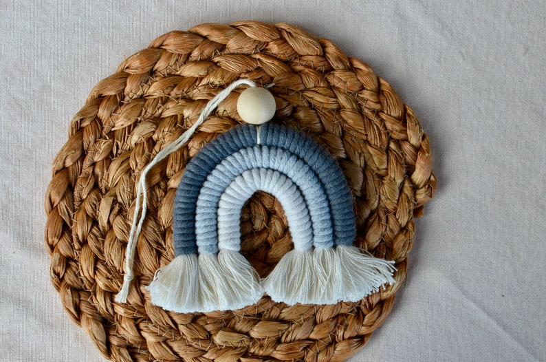 May include: A blue and white ombre rainbow wall hanging with white tassels. The rainbow is made of yarn and has a wooden bead at the top.