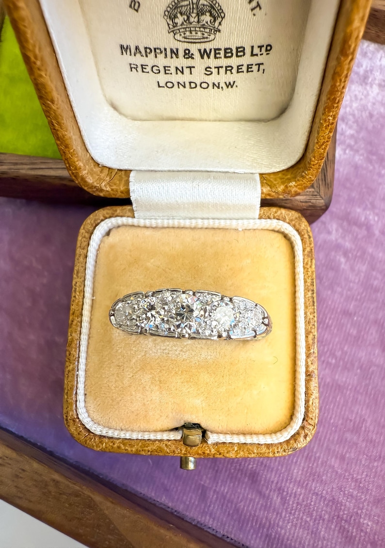 Op de afbeelding: Een antieke platina ring met vijf ronde diamanten, gepresenteerd in een vintage Mappin & Webb Ltd. sieradendoosje. Het doosje is gevoerd met cr&egrave;mekleurig fluweel.