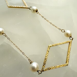 May include: A gold-colored necklace featuring a repeating pattern of diamond-shaped frames and round, white pearls. The chain is delicate, and the diamonds have a textured surface. The pearls are evenly spaced.
