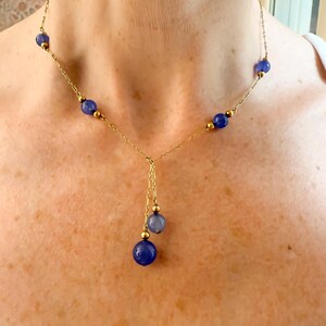 May include: A delicate gold necklace featuring a series of deep blue beads interspersed with smaller gold beads. The necklace has a Y-shaped drop with three additional blue beads. The necklace is worn around the neck.