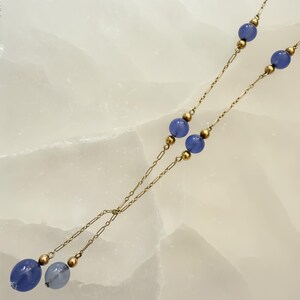 May include: A delicate necklace featuring a gold chain with alternating blue beads and gold accents. The necklace has a Y-shaped design, with larger blue beads at the bottom. The beads are a soft, muted blue color.