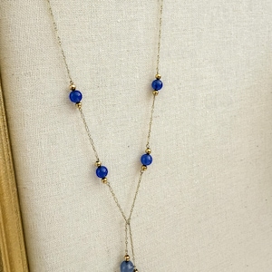 May include: A delicate gold-toned necklace featuring a series of vibrant blue beads. The necklace has a Y-shaped design, with a cluster of blue beads at the bottom. The beads are interspersed with small gold-colored accents.