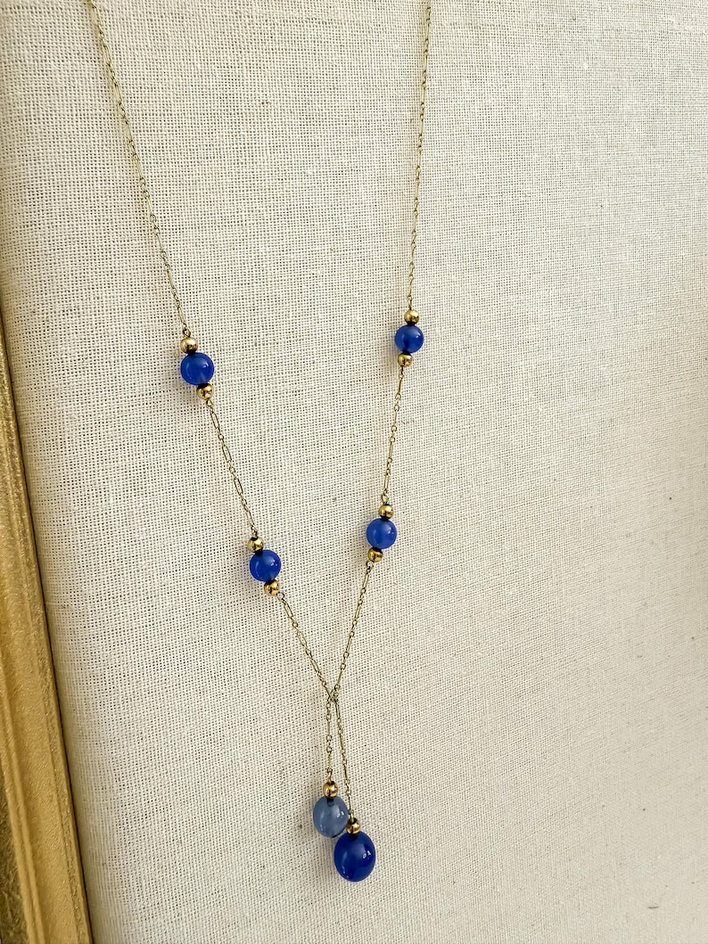 May include: A delicate gold-toned necklace featuring a series of vibrant blue beads. The necklace has a Y-shaped design, with a cluster of blue beads at the bottom. The beads are interspersed with small gold-colored accents.