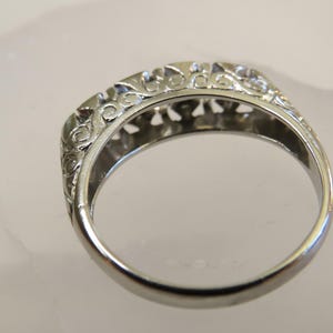 Op de afbeelding: Close-up van een zilveren ring met een sierlijk filigraanontwerp. De ring heeft ingewikkeld krulwerk langs de boven- en zijkanten, waardoor een delicaat en gedetailleerd patroon ontstaat. De ring is waarschijnlijk gemaakt van sterling zilver of een vergelijkbaar metaal.