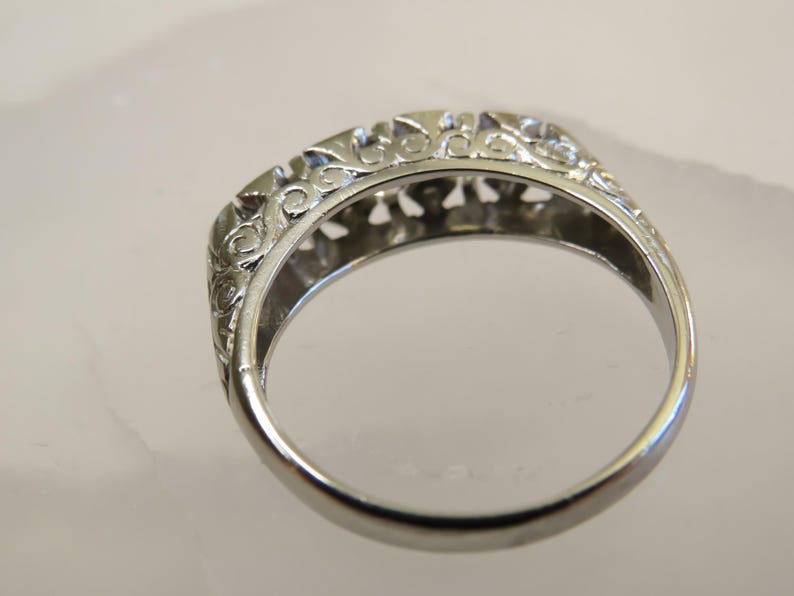 Op de afbeelding: Close-up van een zilveren ring met een sierlijk filigraanontwerp. De ring heeft ingewikkeld krulwerk langs de boven- en zijkanten, waardoor een delicaat en gedetailleerd patroon ontstaat. De ring is waarschijnlijk gemaakt van sterling zilver of een vergelijkbaar metaal.