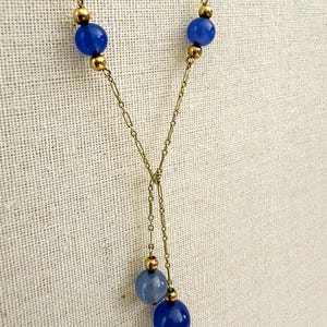 May include: A gold-toned necklace with a Y-shaped design. The necklace features three vibrant blue spherical beads and smaller gold-colored beads. The chain is delicate, with a simple link pattern. The necklace is displayed against a neutral background.