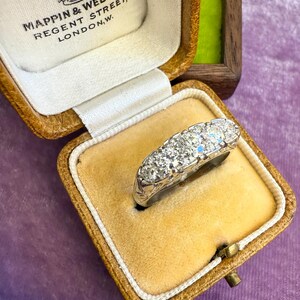 Op de afbeelding: Een vintage diamanten ring, gepresenteerd in de originele Mappin & Webb Ltd. doos. De ring heeft meerdere rond geslepen diamanten gezet in een witmetalen band. De doos is van bruin leer met een cr&egrave;mekleurig satijnen interieur.