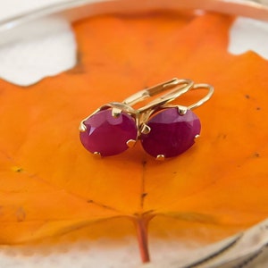 May include: A pair of gold earrings with oval-shaped pink gemstones. The earrings are on a fall leaf.