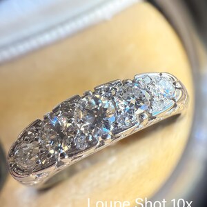 Op de afbeelding: Close-up van een diamanten ring met meerdere rond geslepen diamanten gezet in een witte metalen band. De ring is vergroot afgebeeld, met de tekst "Loupe Shot 10x" zichtbaar.