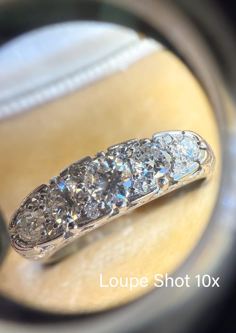 Op de afbeelding: Close-up van een diamanten ring met meerdere rond geslepen diamanten gezet in een witte metalen band. De ring is vergroot afgebeeld, met de tekst "Loupe Shot 10x" zichtbaar.