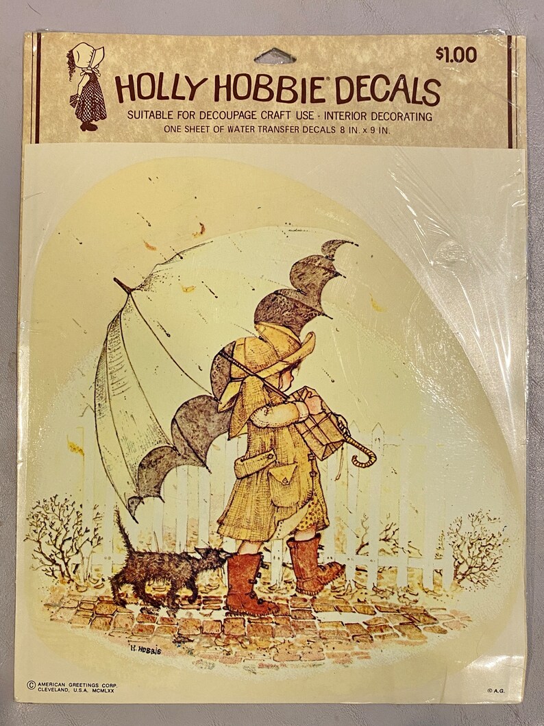 May include: A vintage Holly Hobbie decal sheet featuring a girl walking with a black cat under an umbrella. The decal sheet is suitable for decoupage craft use and interior decorating. It measures 8 inches by 9 inches.