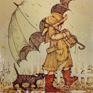 May include: A girl in a yellow coat and brown boots walks with a black cat in the rain. She is holding a brown package and an umbrella. The scene is painted in a vintage style with a white picket fence in the background.