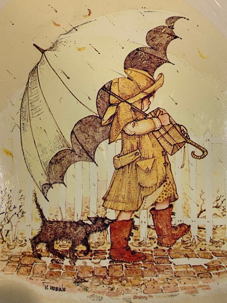 May include: A girl in a yellow coat and brown boots walks with a black cat in the rain. She is holding a brown package and an umbrella. The scene is painted in a vintage style with a white picket fence in the background.