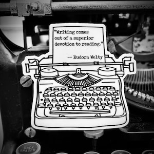 May include: Black and white illustration of a vintage typewriter with the quote "Writing comes out of a superior devotion to reading." - Eudora Welty.