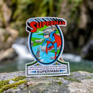 May include: A sticker featuring Superman fishing with the text "Cast a Kryptonite Clouser on a Solar Flare Rod. set the hook and lift that Fish Up. Up, and Away!" and "SUPERMAN" at the top and bottom.