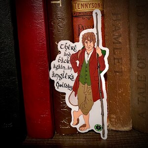 May include: A sticker featuring a cartoon illustration of a man with a beard and a fishing rod. The man is wearing a red coat, a green vest, and brown pants. The sticker has the text "There and back again, an angler's holiday" written in a stylized font.