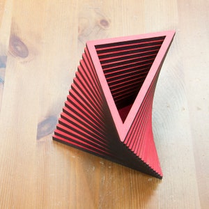 May include: A red and black geometric sculpture made of stacked triangles. The sculpture is shaped like a vase or a container.