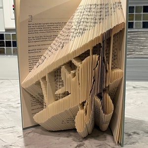 May include: A book with pages folded into a three-dimensional sculpture of a plane. The book is open and the sculpture is visible from the side. The book cover is light blue with white text. The text on the cover reads "Start Late, Finish Rich. Copyright © 2005 by David Bach. All rights reserved."