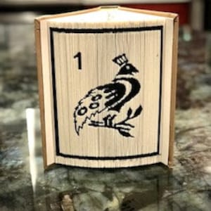 May include: A book folded into a three-dimensional sculpture of a bird with black and white details. The sculpture is numbered "1" in the upper left corner.