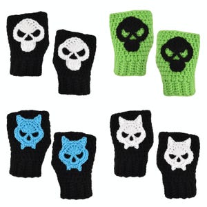 Könnte beinhalten: Gehäkelte Fingerhandschuhe in Schwarz und Grün, jeweils mit einem Totenkopf- oder Katzenmuster. Die Totenkopfdesigns sind weiß oder schwarz, und die Katzenmotive sind blau oder weiß. Handgefertigte Handschuhe, geeignet für verschiedene Anlässe.