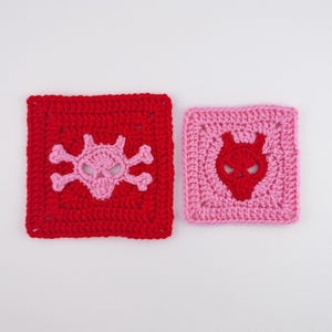 May include: Two crocheted squares. One is red with a pink skull and crossbones design. The other is pink with a red devil face design. Both are square shaped and have a textured appearance.