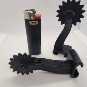 May include: Two black plastic cowboy spurs with a star-shaped rowel and a black Bic lighter.