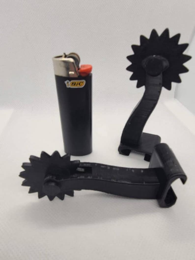 May include: Two black plastic cowboy spurs with a star-shaped rowel and a black Bic lighter.
