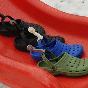May include: Three pairs of clogs with a cowboy boot spur attached to the strap. The clogs are black, blue, and green.