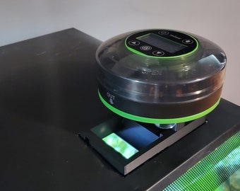 May include: Black and green automatic fish feeder with a clear lid and a digital display. The feeder is mounted on top of a black aquarium.