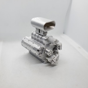 Puede incluir: Un modelo de motor grande impreso en 3D de color plateado con una gran toma de aire en la parte superior. El motor tiene la palabra "MOROSO" impresa en el lateral.