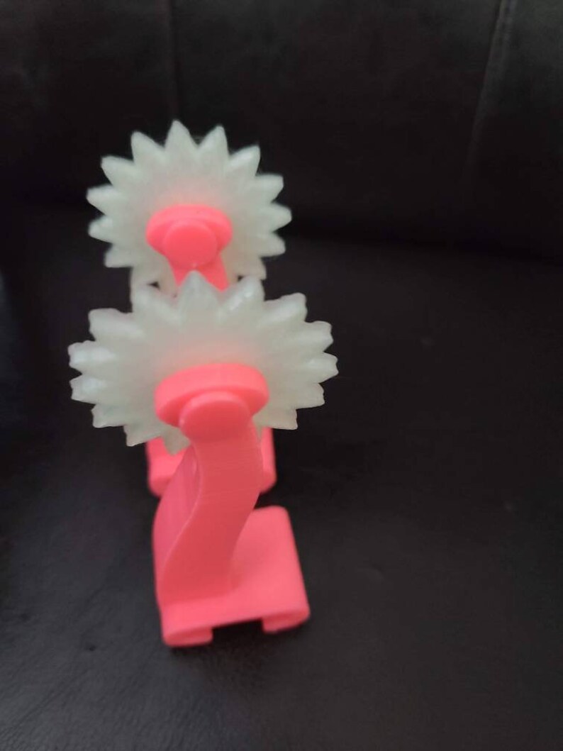 May include: A pink plastic tool with two white, star-shaped wheels. The tool is used for creating decorative patterns in clay or fondant.