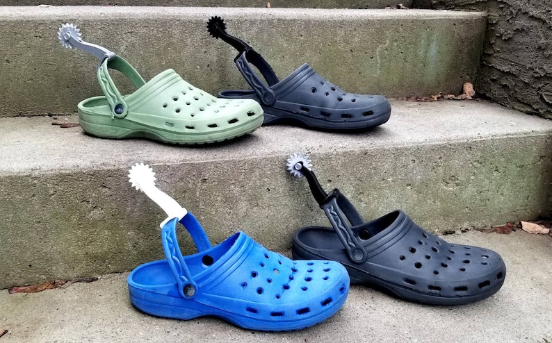 May include: Four pairs of colorful clogs with a spur attached to the back strap. The clogs are green, black, blue, and black. The spurs are silver, black, white, and black.