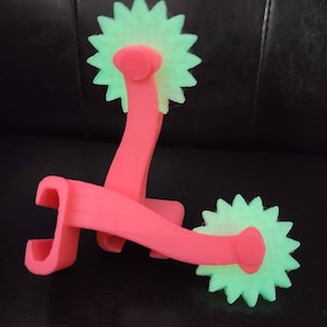 May include: Two pink plastic rolling tools with green star-shaped wheels. The tools are designed for crafting and creating patterns in clay or dough.