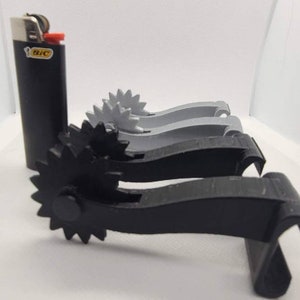 May include: Three 3D printed black and gray gear-shaped objects with a black lighter in the background.