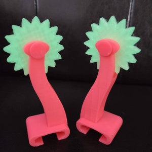 May include: Two pink plastic tools with green star-shaped wheels. The tools have a handle that curves up and then down to form a hook.
