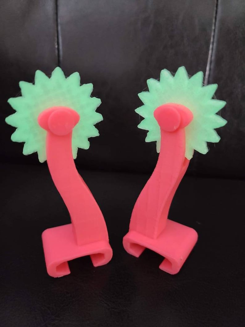 May include: Two pink plastic tools with green star-shaped wheels. The tools have a handle that curves up and then down to form a hook.