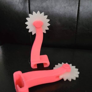May include: Two pink plastic tools with white wheels. The wheels have a starburst design. The tools are used for quilting or sewing.