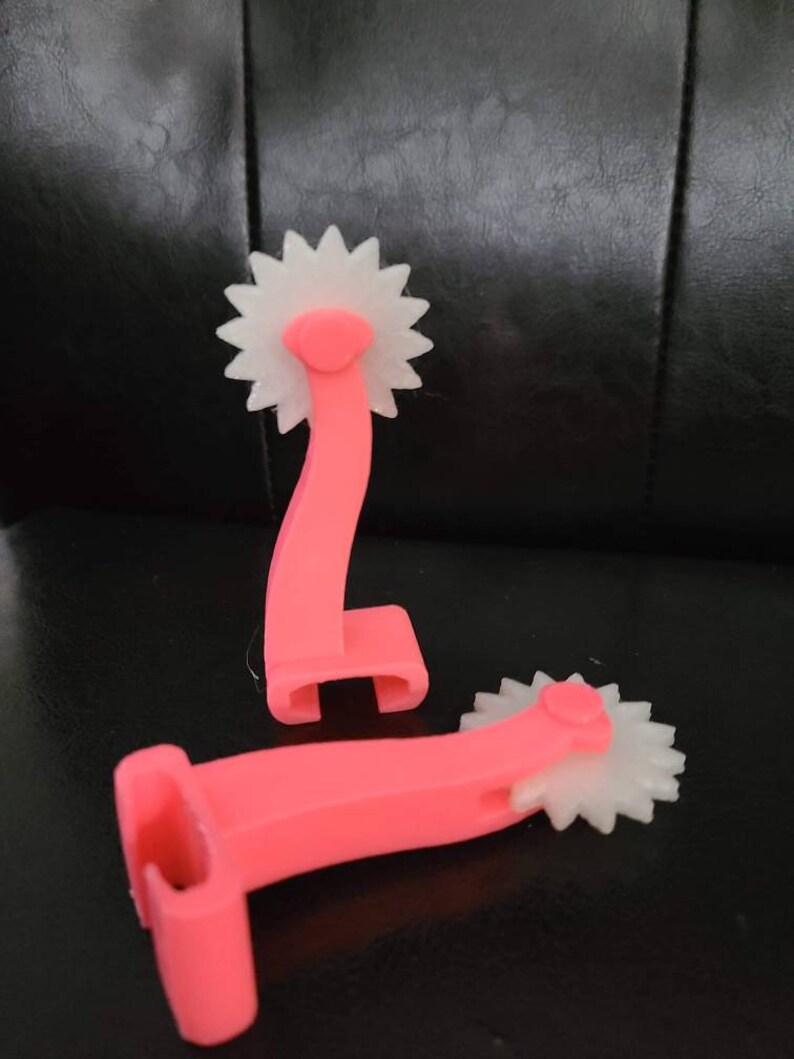 May include: Two pink plastic tools with white wheels. The wheels have a starburst design. The tools are used for quilting or sewing.