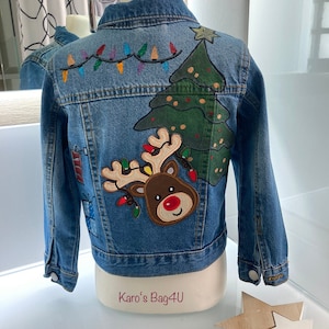 Könnte beinhalten: Eine blaue Jeansjacke mit einem Weihnachtsbaum, einem Rentier und einer Lichterkette, die auf der Rückseite gestickt sind. Der Text "Karo's Bag4U" ist auf der Unterseite der Jacke aufgedruckt.