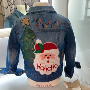Könnte beinhalten: Eine blaue Jeansjacke, verziert mit einem Weihnachtsbaum, dem Weihnachtsmann und einer Lichterkette. Die Weihnachtsmann-Applikation trägt den Text "Ho Ho Ho".
