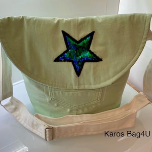 Könnte beinhalten: Eine hellgrüne Canvas-Tasche mit einem weißen Trageriemen und einem großen grün-blau-schwarzen Stern aus Pailletten. Die Tasche hat eine Klappe mit einer Tasche und der Text "Karos Bag4U" ist unten im Bild gedruckt.